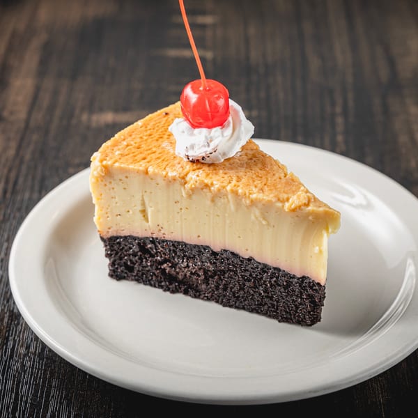 A slice of Mexican flan cake with chocolate base, topped with whipped cream and a cherry.