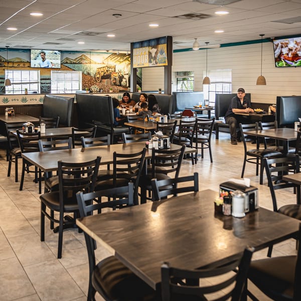 Interior of Taqueria Los Agaves with customers dining at tables and booths, featuring a desert mural.
