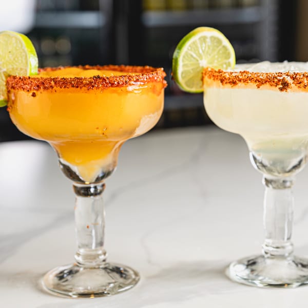 Two margaritas, one mango and one classic, with chili-lime rims and lime wedges.