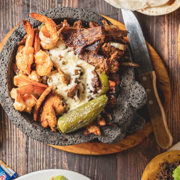 Molcajete with grilled shrimp, steak, melted cheese, and a jalapeño, served on a wooden board.