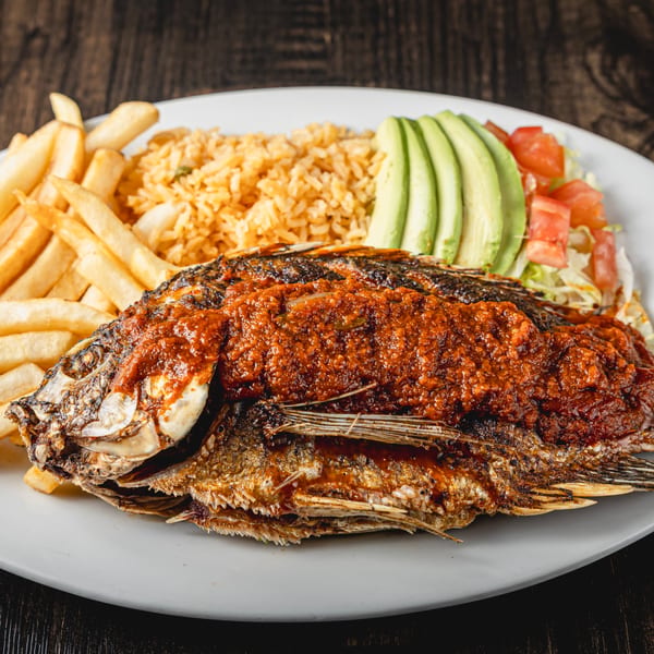 Whole fried fish topped with red sauce, served with rice, fries, avocado, and salad.