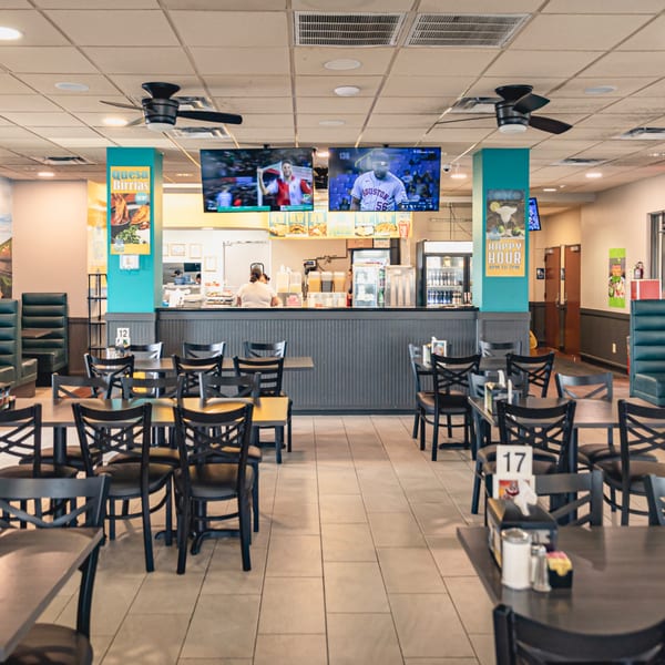 Interior of Taqueria Los Agaves, with empty tables and chairs, a counter, and TVs showing sports.