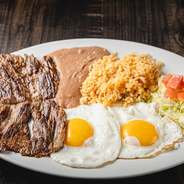 Grilled steak, two fried eggs, refried beans, Mexican rice, and a side salad on a white plate.