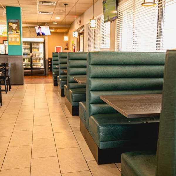 Interior of Taqueria Los Agaves with rows of green booths, tables, and tiled flooring.