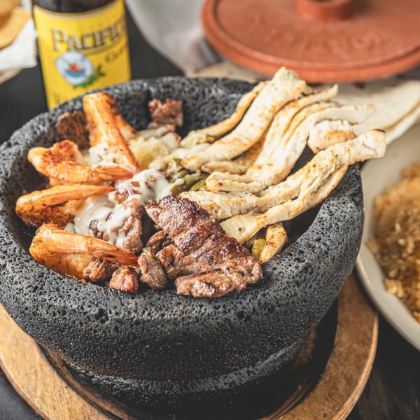 Molcajete dish with grilled steak, shrimp, and tortillas, served with a Pacifico beer.