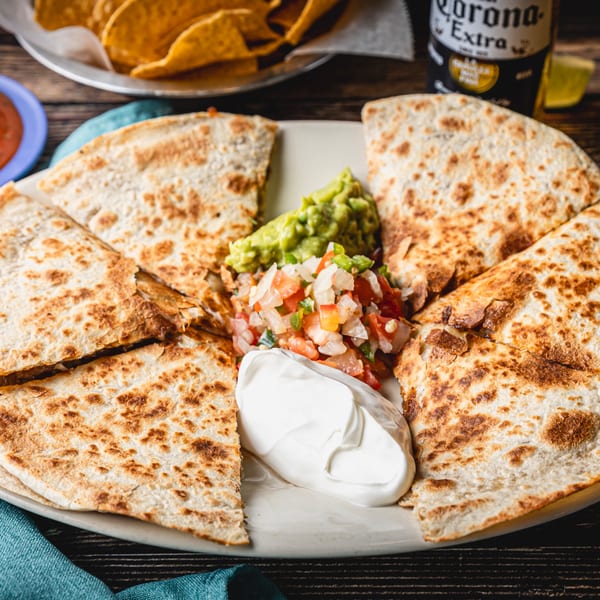 Four quesadilla slices with guacamole, pico de gallo, and sour cream, with tortilla chips and beer.