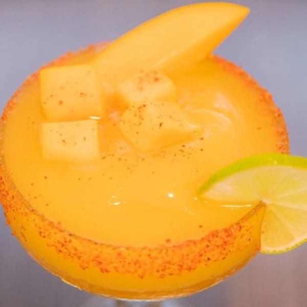 Mango margarita with chili-lime rim, topped with mango slices, cubes, and a lime wedge.
