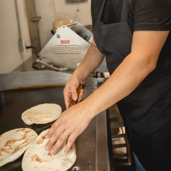 Chef in black apron cooking fresh tortillas on a flat-top grill at Taqueria Los Agaves.