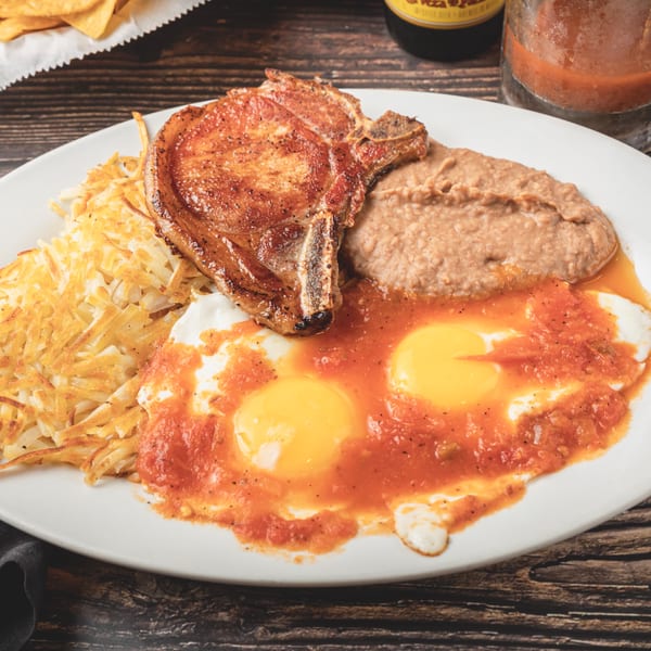 Taqueria Los Agaves' Mexican breakfast plate with pork chop, hash browns, refried beans, and huevos rancheros.