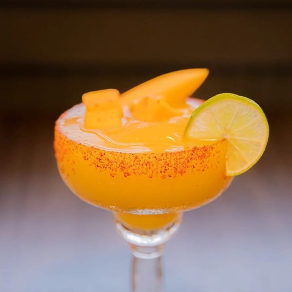 A mango margarita in a salt-rimmed glass, garnished with mango slices and a lime wedge.