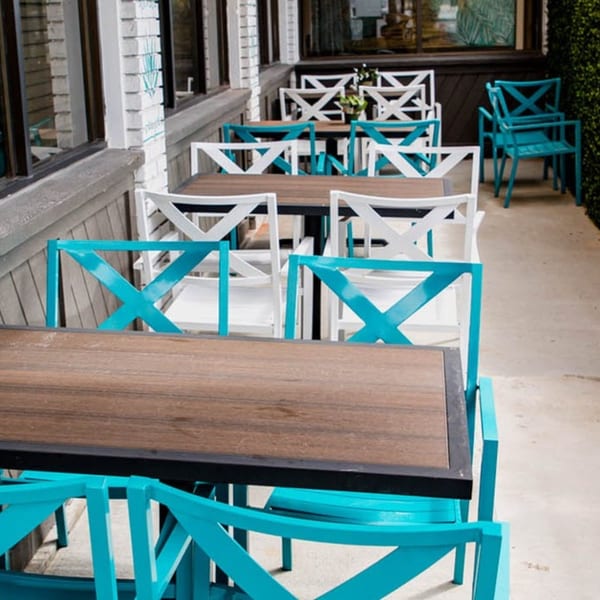 Outdoor patio seating with teal and white chairs and dark wood tables at Taqueria Los Agaves.