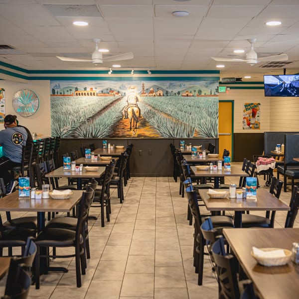 Interior of Taqueria Los Agaves restaurant with tables, chairs, and a large mural of an agave field.