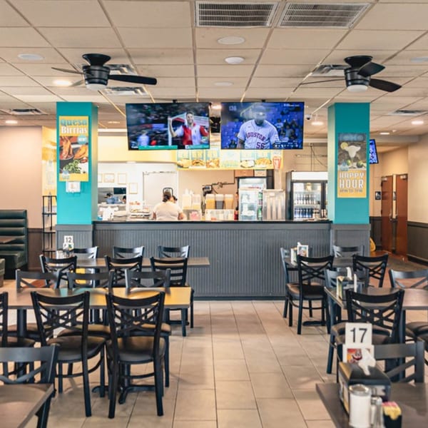 Interior of Taqueria Los Agaves with empty tables, a service counter, and TVs showing sports.