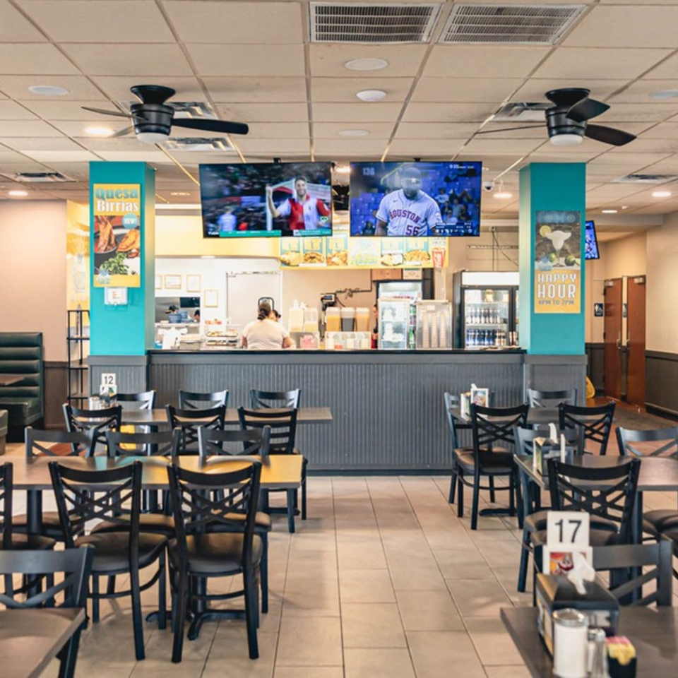 Interior of Taqueria Los Agaves with empty tables, a service counter, and TVs showing sports.