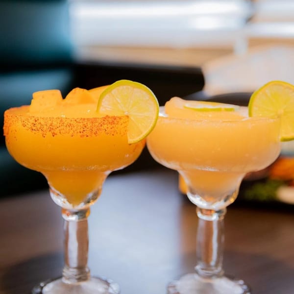 Two mango margaritas with lime slices and chili-salt rims on a dark table at Taqueria Los Agaves.