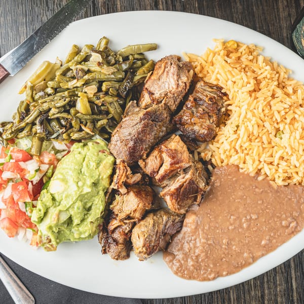 Mexican carnitas plate with rice, refried beans, guacamole, pico de gallo, and grilled nopales.