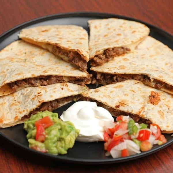 Six triangular quesadilla slices filled with meat, served with guacamole, sour cream, and pico de gallo.