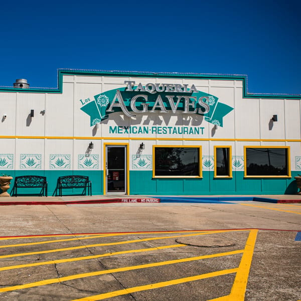 Exterior of Taqueria Los Agaves, a Mexican restaurant with a white and teal facade and yellow trim.