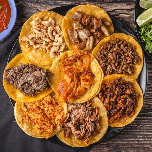A black platter filled with eight different kinds of Taqueria Los Agaves tacos, with salsa and lime.