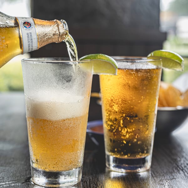 Modelo beer pouring from a bottle into a frosty glass with lime, next to another full beer.