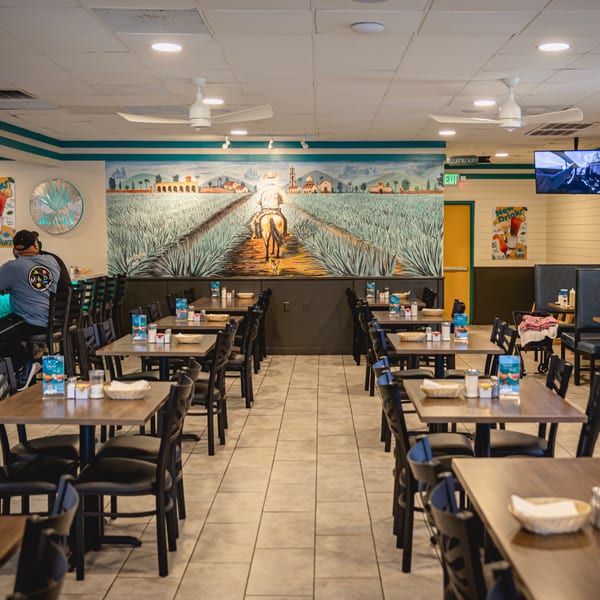 Interior of Taqueria Los Agaves restaurant with tables, chairs, and a large agave field mural.